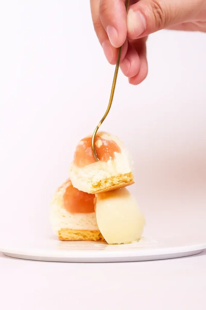 Peach Shaped Pastry 9 A fork cutting through a layered peach shaped cookie filled with cream and peach gelée