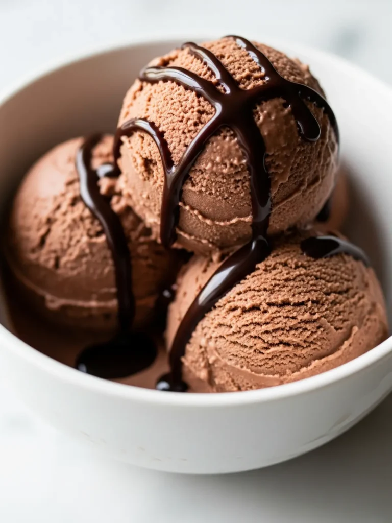 A minimalist white bowl holding three smooth scoops of rich chocolate protein ice cream, elegantly topped with a glossy chocolate syrup drizzle, set against a bright marble countertop.