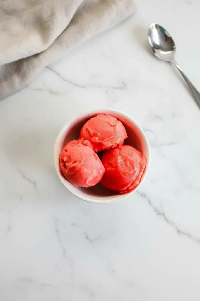 A spoon creating a perfect curl in a pint of dense sorbet, demonstrating the ideal texture of this ninja creami frozen fruit recipe.